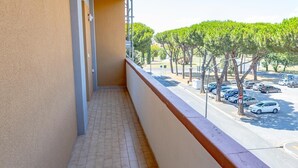 Un balcón con suelo de baldosas, con vistas a un estacionamiento con coches y árboles.