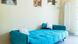 Un sofá color turquesa con dos almohadas, un radiador y una obra de arte en la pared.