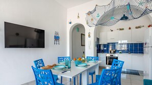 A dining area with blue chairs, a white table, and a kitchen in the background. - Casa Celeste 100m From Sea (Porto Cesareo)