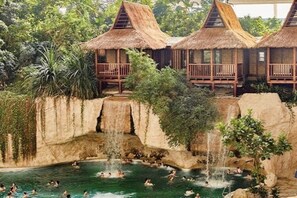 Ein Resort mit strohgedeckten Bungalows, einem zentralen Pool mit Wasserfällen und üppiger Vegetation.