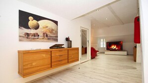 A modern living room with a wooden cabinet, a large painting of a planet, and a fireplace. - Apartment SL Lounge, Luebben (Lübben (Spreewald))
