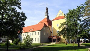 A building with a red roof and a tower, surrounded by green grass and trees. - Apartment SL Lounge, Luebben (Lübben (Spreewald))