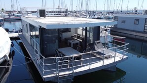 Una estructura flotante con cerramiento de vidrio, un pequeño comedor y una zona de estar con mesa y sillas.