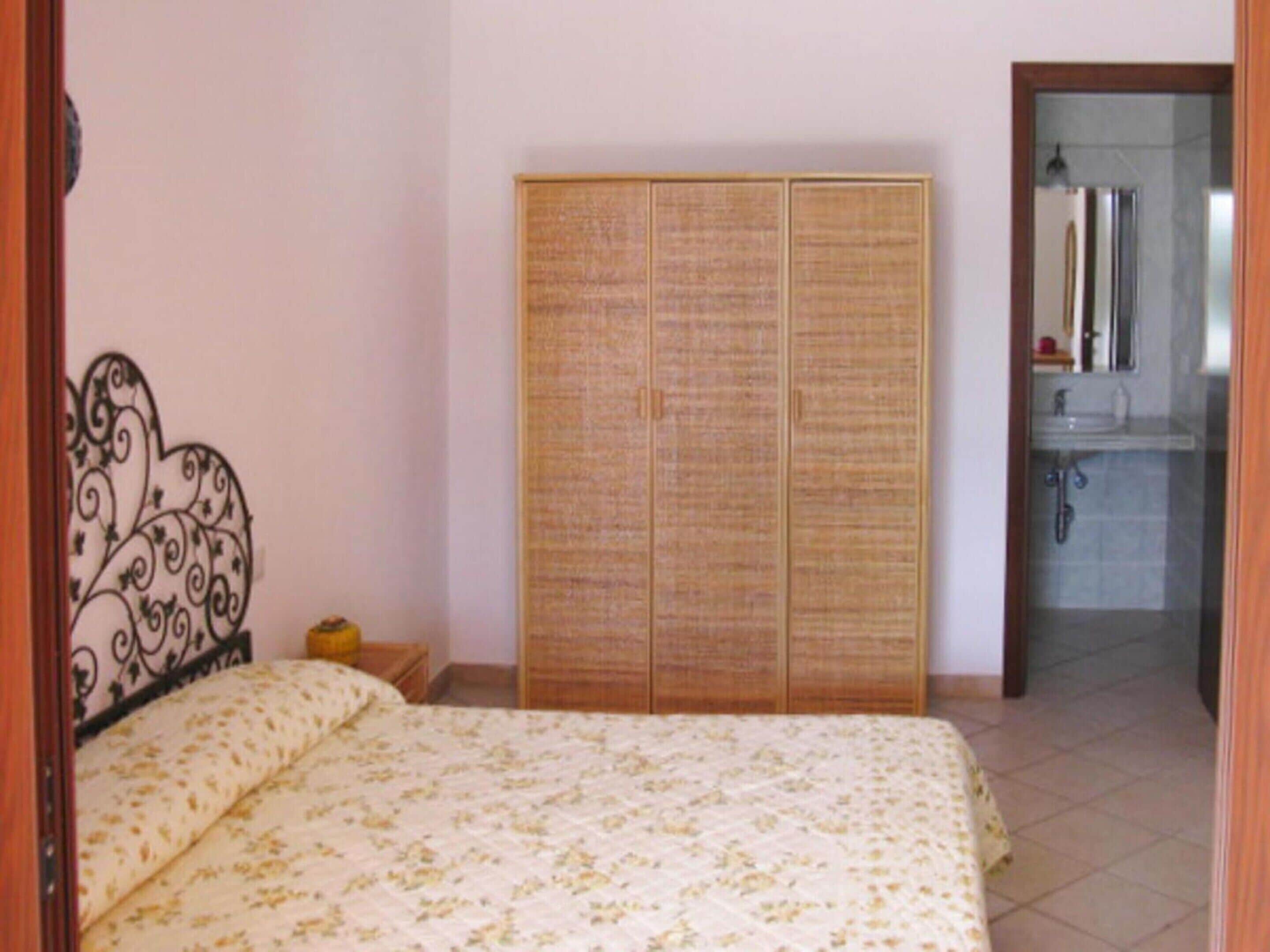 Una camera da letto con un letto, un armadio e un bagno visibile attraverso una porta aperta.