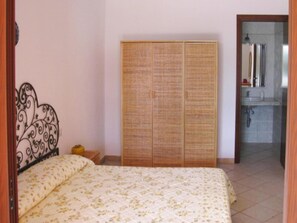 A bedroom with a bed, a wardrobe, and a bathroom visible through an open door. - Apartment on Costa Rei With Sea View (Muravera)