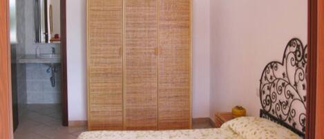 A bedroom with a bed, a wardrobe, and a bathroom visible in the background.