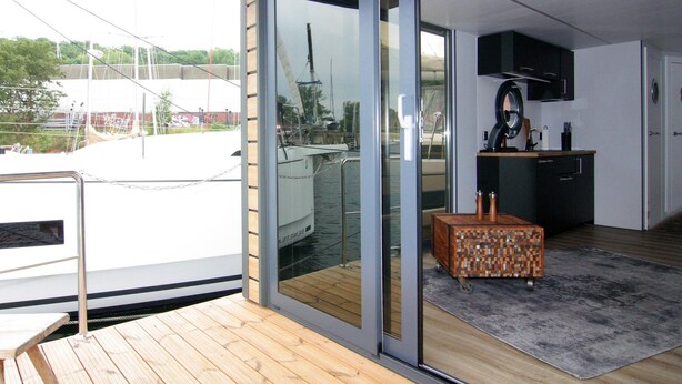 A modern kitchen with a wooden island, a large window with a view of a boat, and a sliding glass door leading to an outdoor deck. - Hausboot Leni, Flensburg (Flensburg)