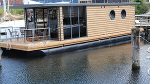 A wooden boat with a deck, seating, and a covered area with windows. - Hausboot Leni, Flensburg (Flensburg)