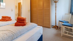 A bedroom with two beds, a wooden wardrobe, a chair, and a coat rack. - Ferienwohnung in St. Peter-ording (St. Peter-Ording)