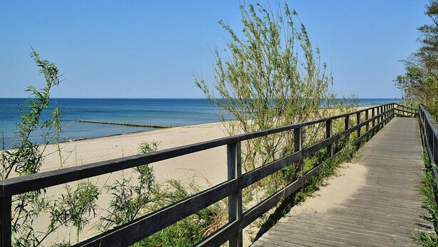 A wooden boardwalk leading to a beach with clear blue water and a sandy shore. - Apartment, Kolobrzeg (Kolobrzeg)