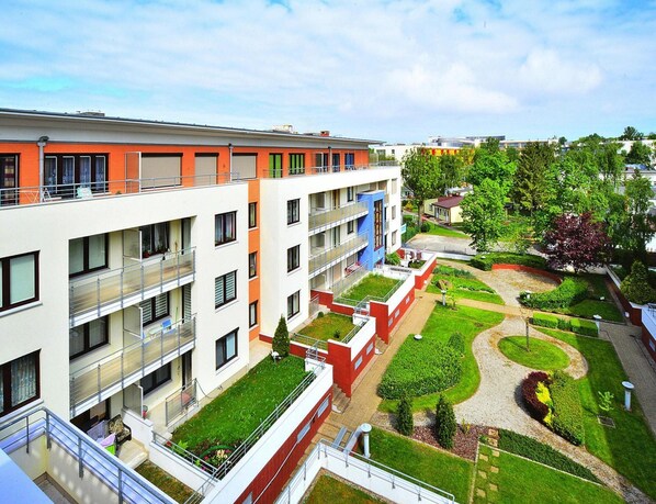Un edificio residenziale a più piani con balconi, un cortile centrale con vegetazione e un cielo sereno.