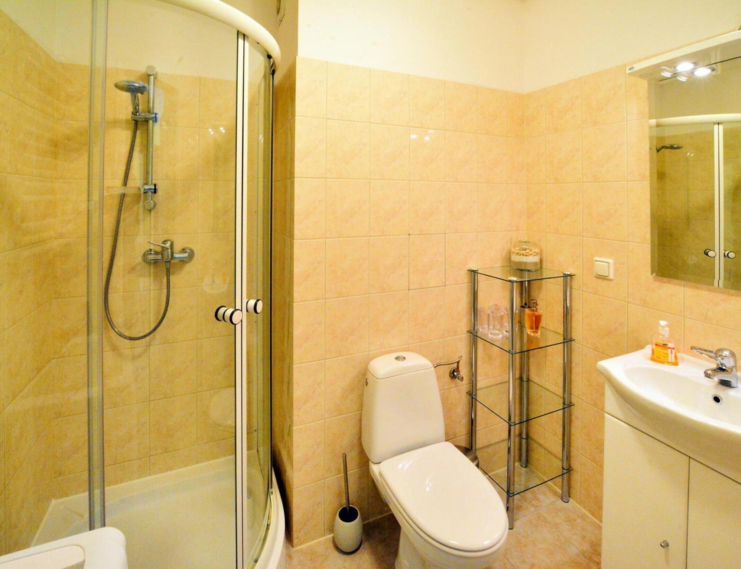 A bathroom with a glass-enclosed shower, a toilet, a glass shelf with toiletries, and a sink with a mirror above it.