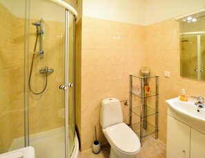Un bagno con doccia vetrata, un water, uno scaffale in vetro con articoli da toilette e un lavandino con uno specchio sopra.