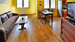 A living room with a sofa, a dining table with chairs, a television, and a kitchen area with cabinets and a refrigerator. - Apartment, Kolobrzeg (Kolobrzeg)