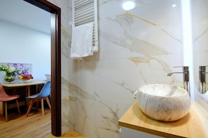 A bathroom with a marble wall, a wooden vanity, and a round sink.