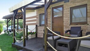 A covered outdoor seating area with wicker furniture and a wooden deck. - Holiday Home Miedzywodzie Near Sandy Beach (Dziwnów)