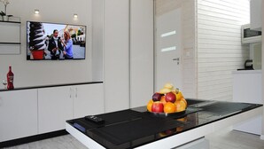 A modern kitchen with a central island, a flat-screen TV mounted on the wall, and a fruit bowl on the island. - Holiday Home Miedzywodzie Near Sandy Beach (Dziwnów)