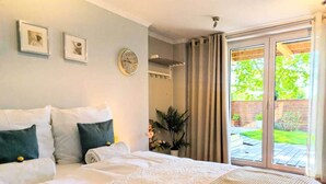 Une chambre à coucher avec un lit, une horloge, une plante et une porte-fenêtre coulissante donnant sur un jardin.