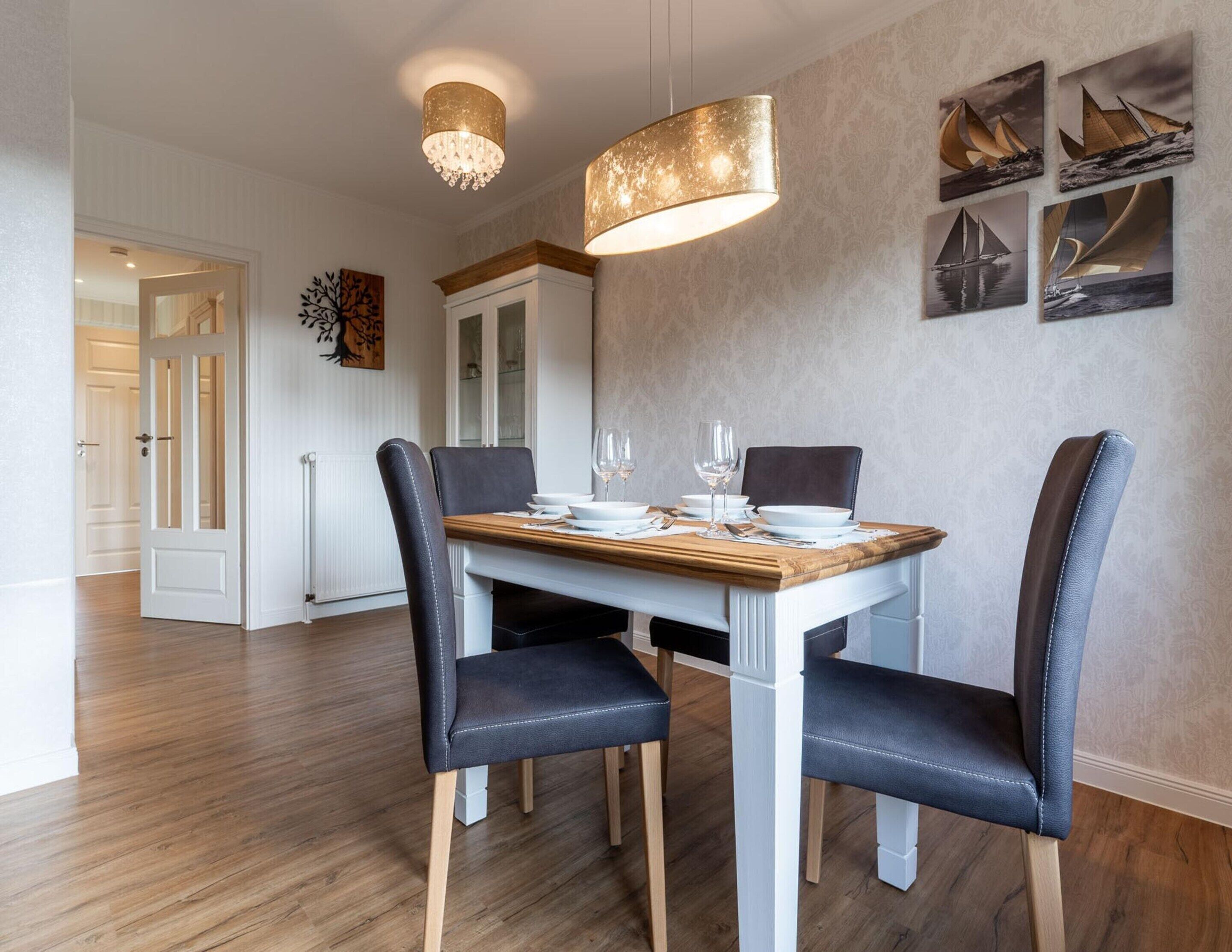 A dining area with a wooden table, four upholstered chairs, and a chandelier.