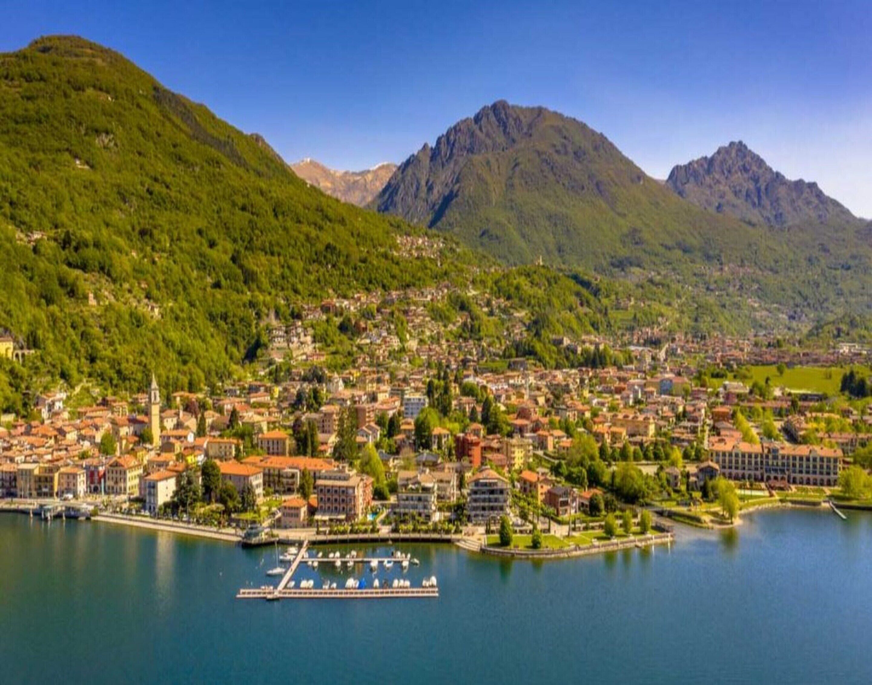 Een kustplaatsje met een jachthaven, omringd door bergen en weelderige groene begroeiing.