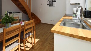 Et moderne køkken med en trætrappe, et spiseområde med et bord og stole, samt en vask med kaffemaskine.