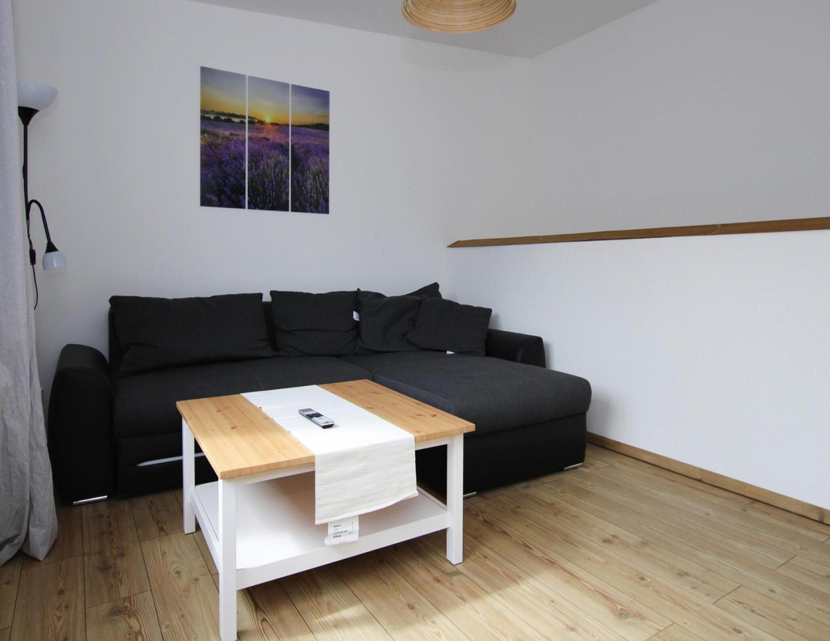 Una sala de estar moderna con un sofá negro, una mesa de centro de madera y una pared blanca con una pintura de atardecer.