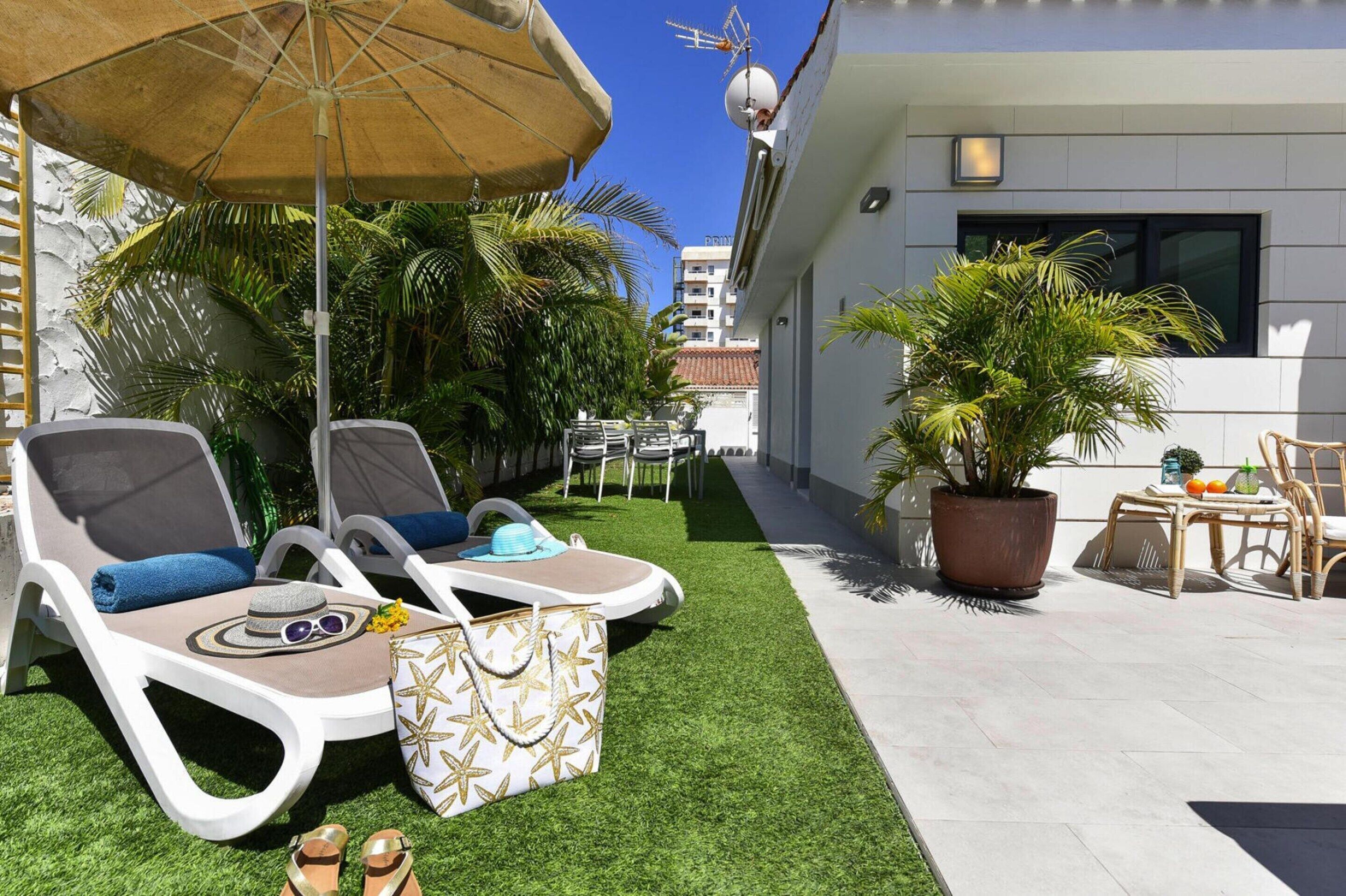 Un espacio lounge moderno al aire libre con tumbonas, una sombrilla grande y una planta en maceta.