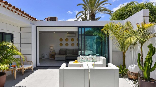 An outdoor living area with white sofas, a dining table, and potted plants.