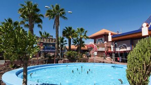 A pool surrounded by palm trees and buildings with signage.