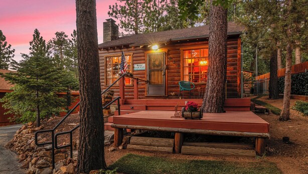 A rustic log cabin with a porch, a flag, and a sign indicating it is a historic site.
