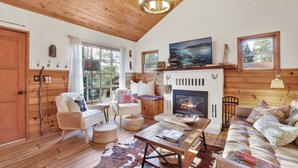 A cozy living room with a fireplace, wooden floors, and a large window.