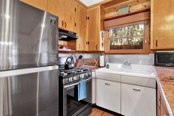 A kitchen with wooden cabinets, a stainless steel refrigerator, a gas stove, and a white sink. - THE Nest ON Towne Trail #2480 (Big Bear Lake)