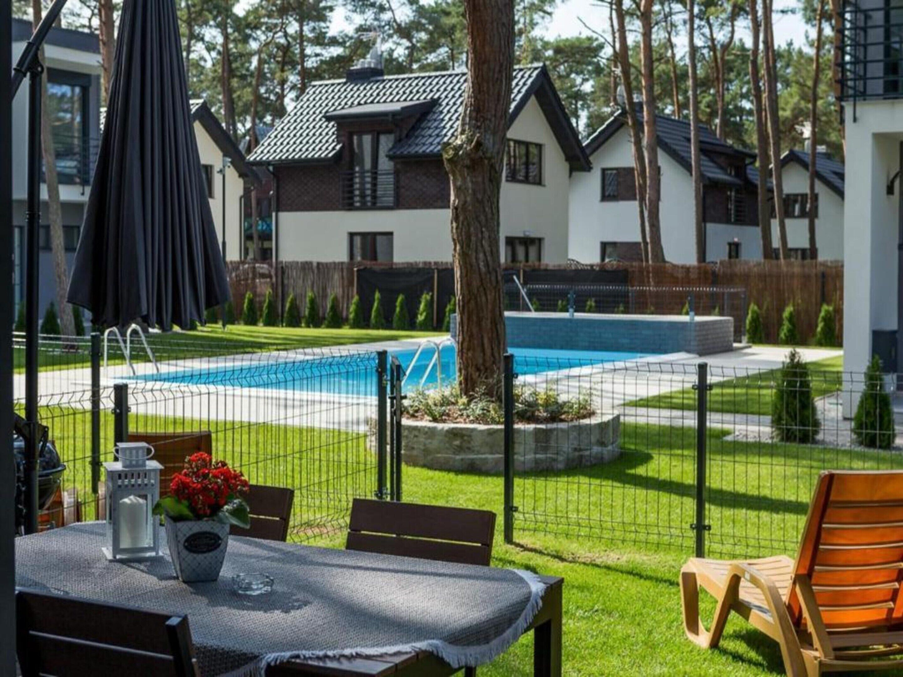 A pool area with a table and chairs, surrounded by a fence and trees.