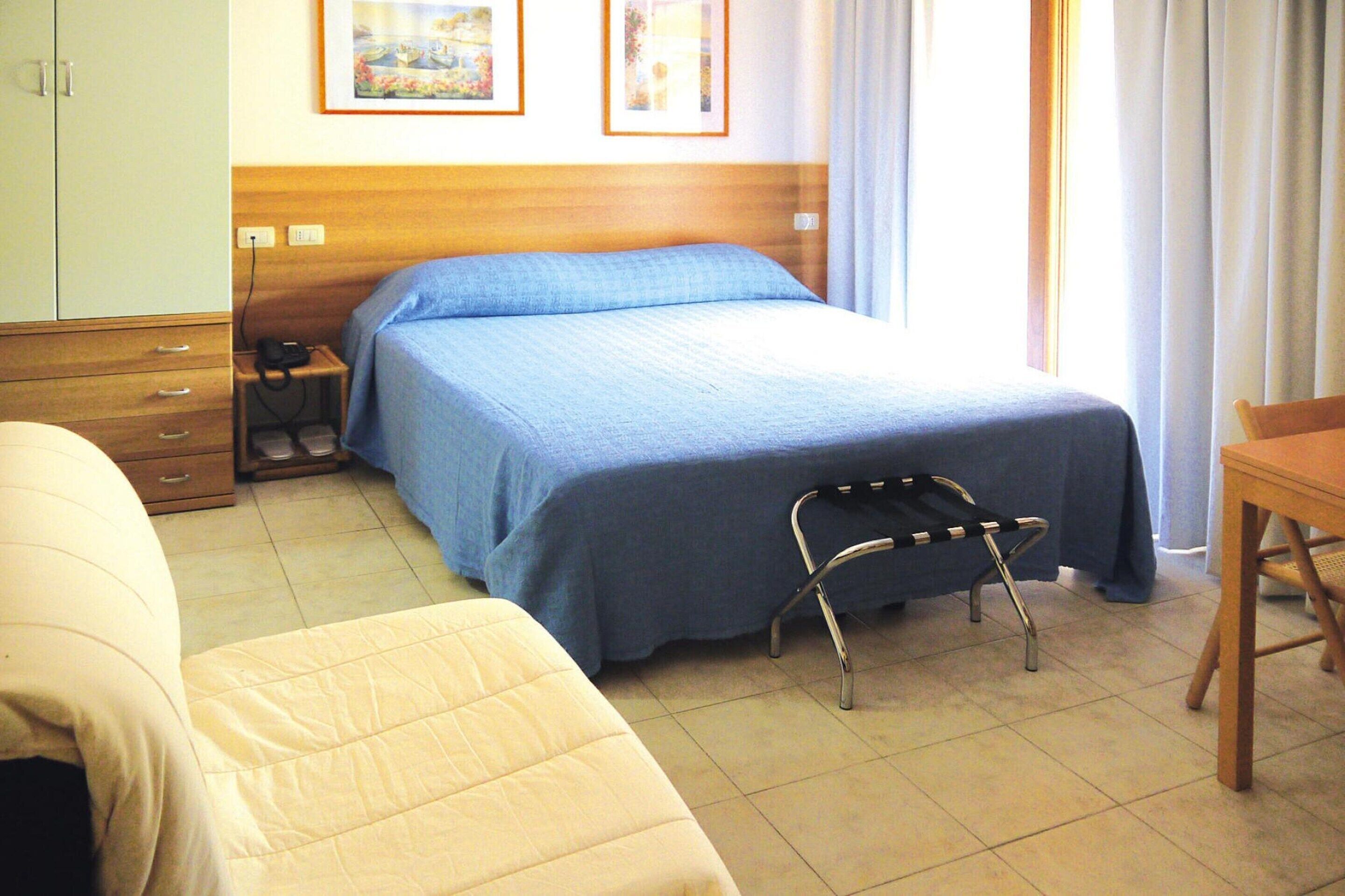 Habitació d'hotel amb llit, cadira, escriptori i armari.