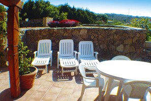 A patio with white chairs and a table, stone wall, and potted plants. - Apartment in Palau Near Surfing Paradise (Palau)