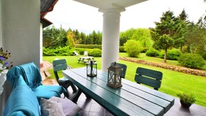 A covered patio with a wooden table and chairs, a bench, and a view of a well-maintained garden. - Large Holiday Villa With Fireplace and Garden (gmina Polanów)