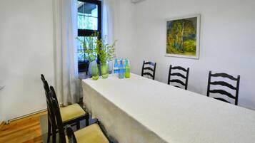 A dining area with a long table, chairs, potted plants, and a painting on the wall.