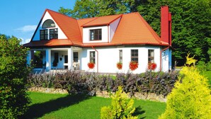 A two-story house with a red roof, white walls, and a stone foundation. - Large Holiday Villa With Fireplace and Garden (gmina Polanów)
