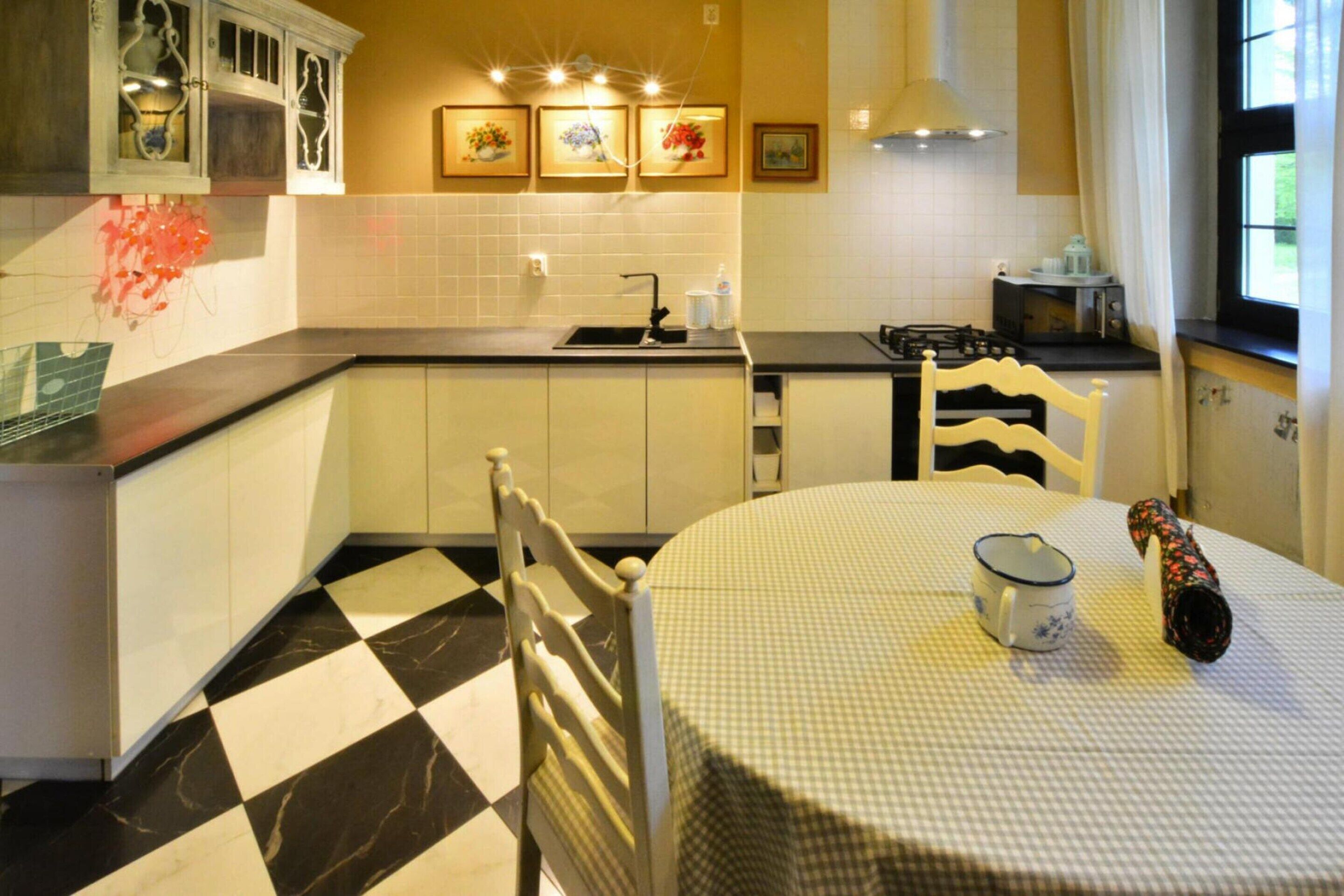 A kitchen with a checkered floor, white cabinets, a stove, and a dining table with a checkered tablecloth.