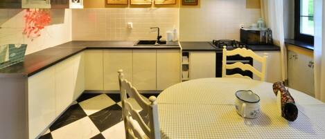 A kitchen with a checkered floor, white cabinets, a stove, and a dining table with a checkered tablecloth.