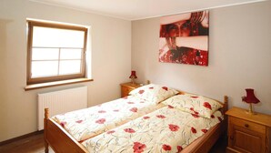 Een slaapkamer met een tweepersoonsbed, een raam, een radiator, een nachtkastje en een wandlamp.