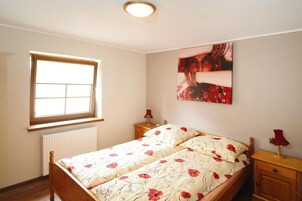 Un dormitorio con cama doble, ventana, radiador, mesita de noche y lámpara de pared.