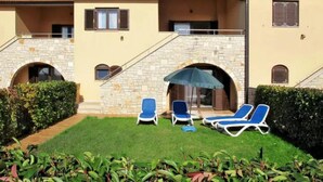 A building with a stone facade, a covered outdoor seating area with blue lounge chairs, and a well-maintained lawn. - Pool House Kristina Near Pore (Kastelir-Labinci)