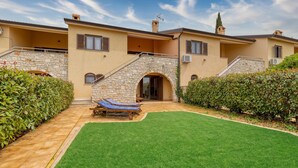 A two-story house with a stone facade, a small garden with a lawn and two lounge chairs, and a clear sky. - Pool House Kristina Near Pore (Kastelir-Labinci)