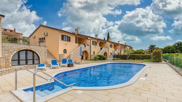 A swimming pool with a stone border, blue lounge chairs, and a stone staircase leading to a building with arched windows. - Pool House Kristina Near Pore (Kastelir-Labinci)