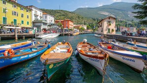 A marina with several boats docked, surrounded by colorful buildings and a mountainous backdrop. - Il Giardino In Montagna Child Friendly (Tenno)