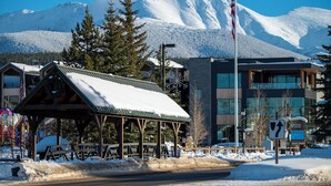 A lodge with a snow-covered roof, a wooden deck, and a view of snow-capped mountains.