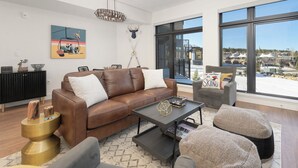 A modern living room with a brown leather sofa, a coffee table, and a view of a snowy landscape through large windows.