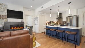 A modern kitchen with a large island, bar stools, a flat-screen TV, and a fireplace.