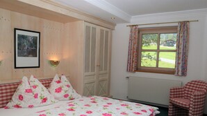 A bedroom with a bed, a chair, a window with curtains, a radiator, and a framed picture on the wall. - Cozy Apartment in Krimml (Krimml)